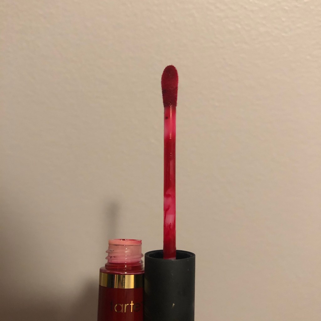 A photo of the Tarte Tarteist Quick Dry Lip Paint in the shade Cheerleader with the tube open to reveal the doe foot applicator.  