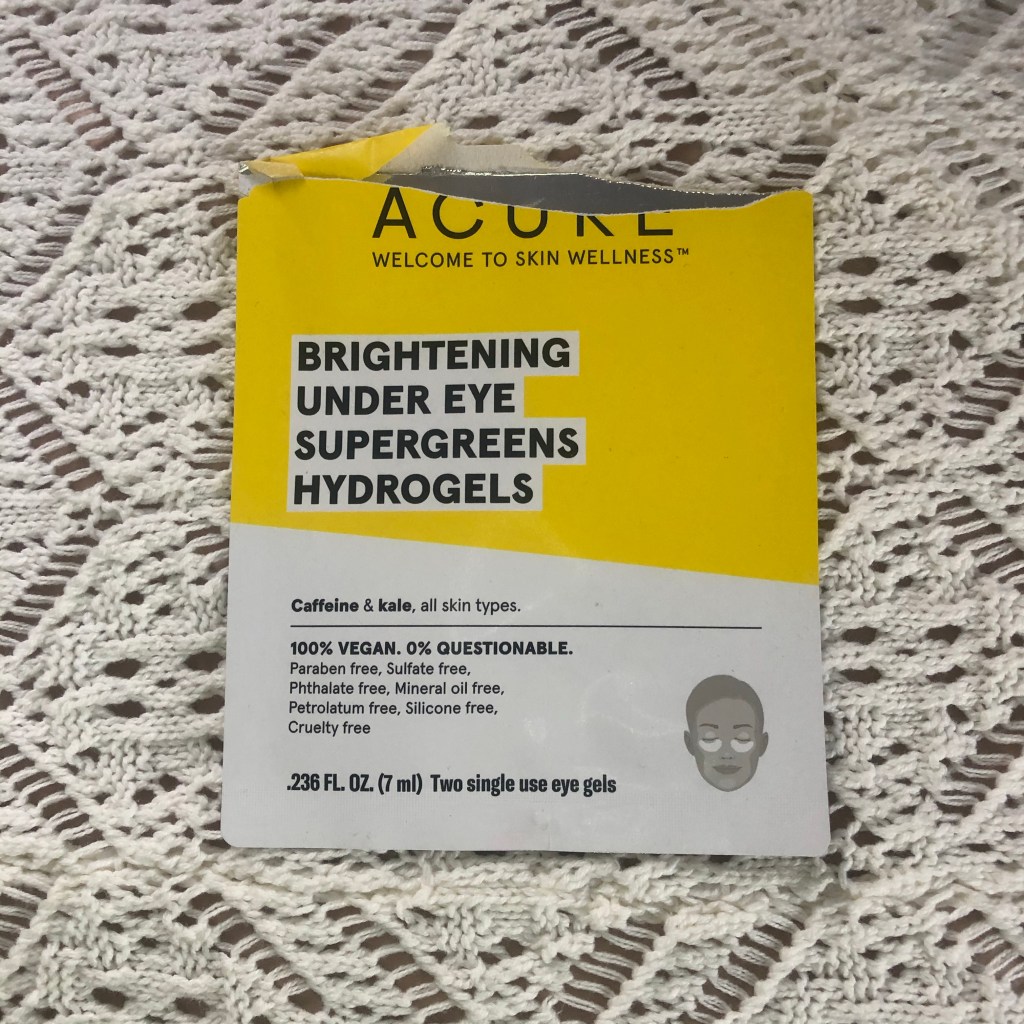 A picture of an opened pack of Acure hydrogel eye patches resting on white crochet background.