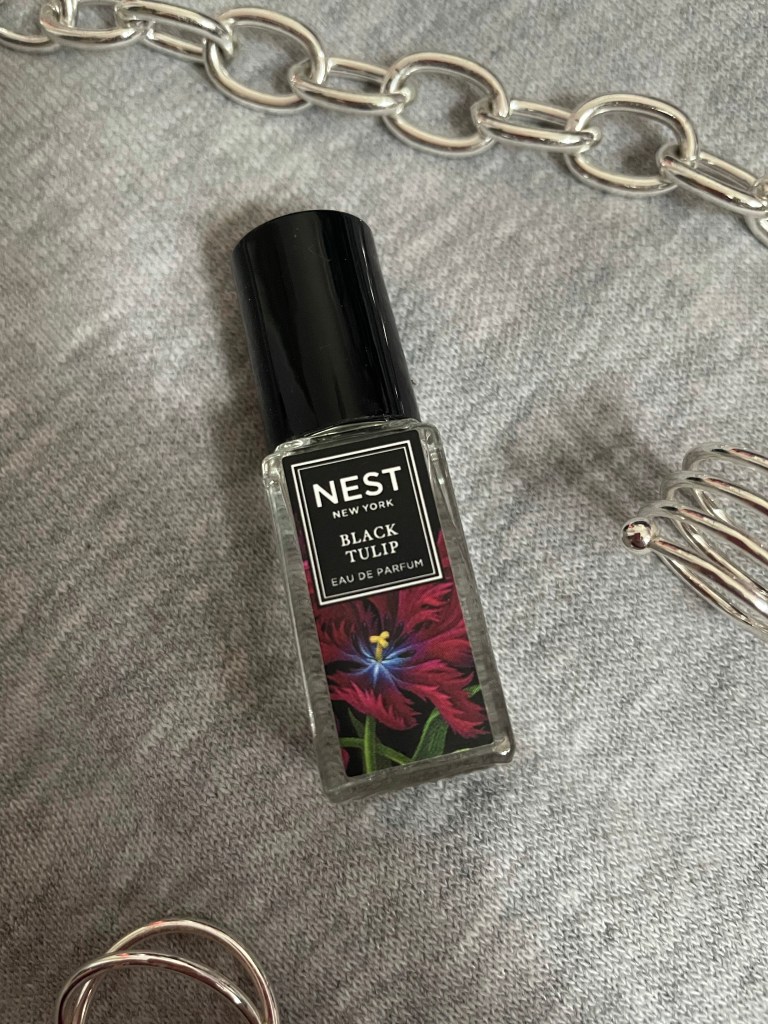 A picture of the travel size fragrance Black Tulip from NEST New York Fragrances on a gray background surrounded by silver jewelry.