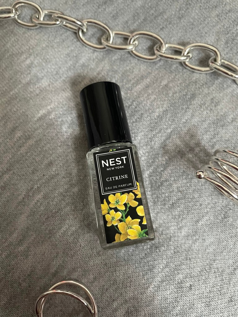 A picture of the travel size fragrance Citrine from NEST New York Fragrances on a gray background surrounded by silver jewelry.